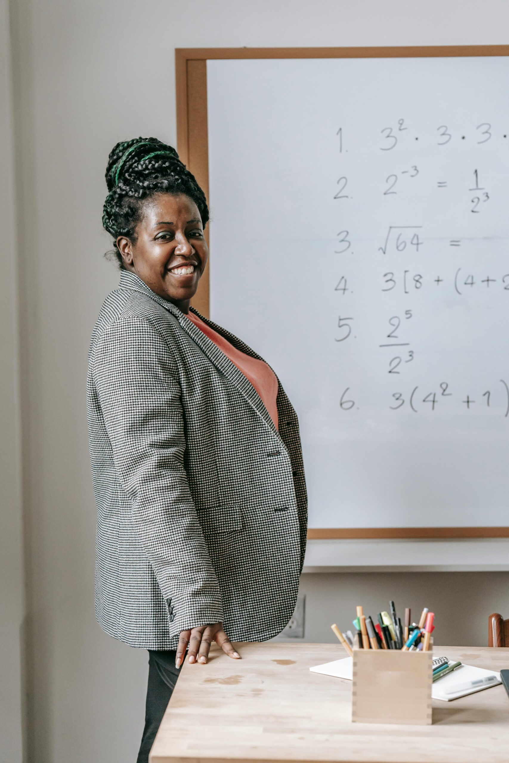 Confident teacher posing by a whiteboard with mathematical equations indoors.